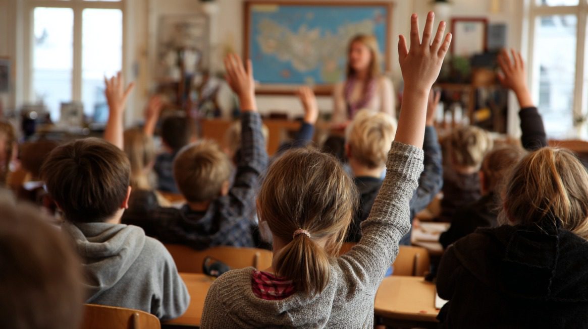 Students raising their hands in a classroom while a teacher stands at the front