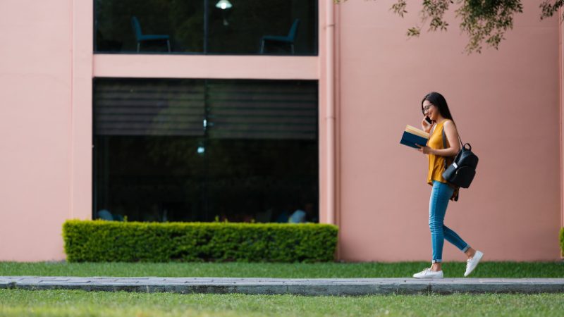 A woman walks outside while reading a book, showing how light movement can support learning