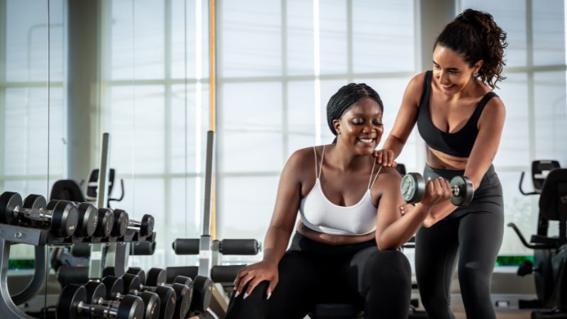 Woman lifts a dumbbell in the gym with help from her trainer