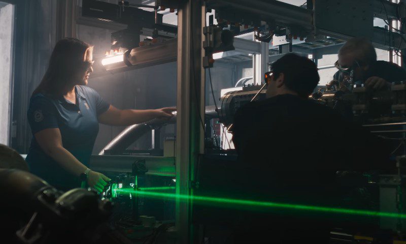 A man and woman collaborate on a machine, focusing on a green laser beam during their work