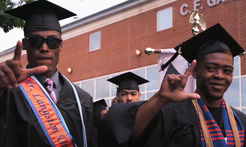 Two men in graduation gowns and caps from Langston University, smiling and giving the peace sign