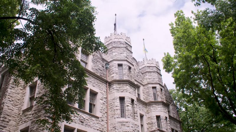 Stone building of the Wharton School at the University of Pennsylvania surrounded by green trees on a bright day